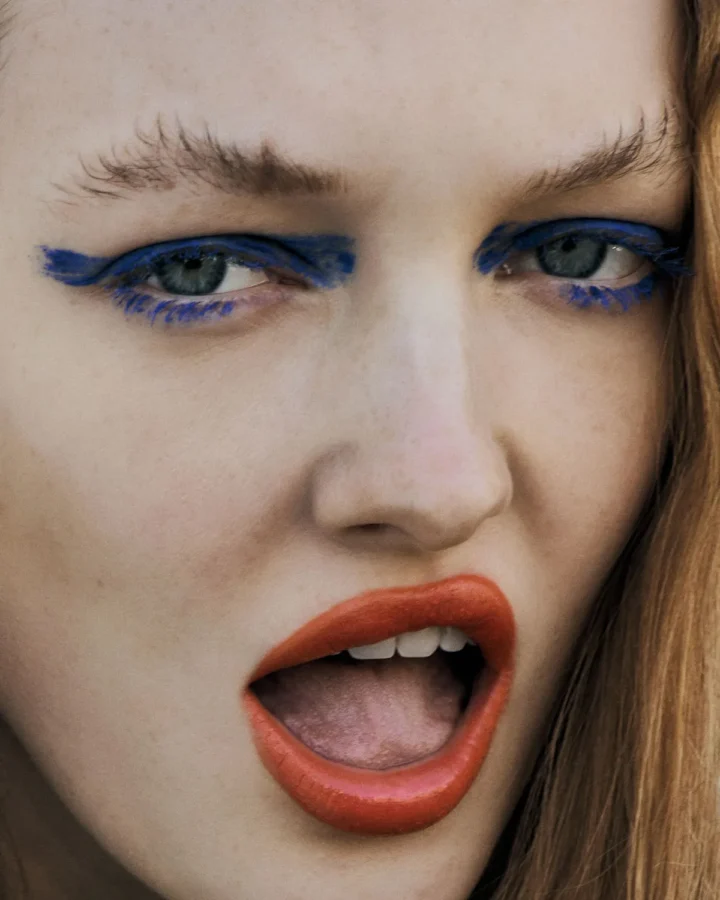 Extreme close-up of a woman's face with vivid blue eyeliner, red lipstick, and expressive facial expression