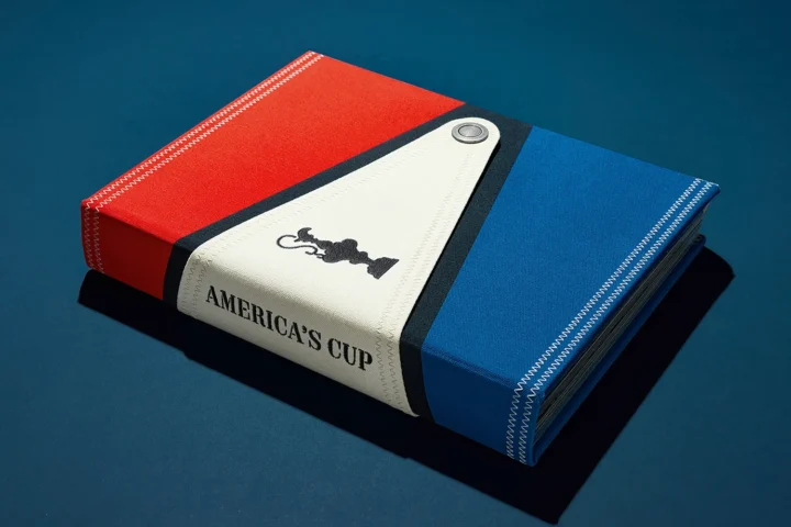 Collector’s edition America’s Cup book lying flat, featuring sailcloth cover with visible spine and trophy print
