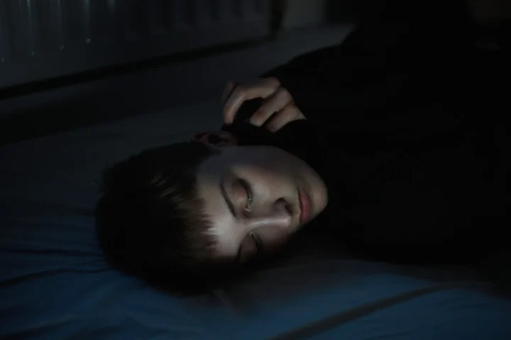 Person lying in shadow on a pillow wearing a dark garment, from the 2025 series “Caroline” by Tia Liu